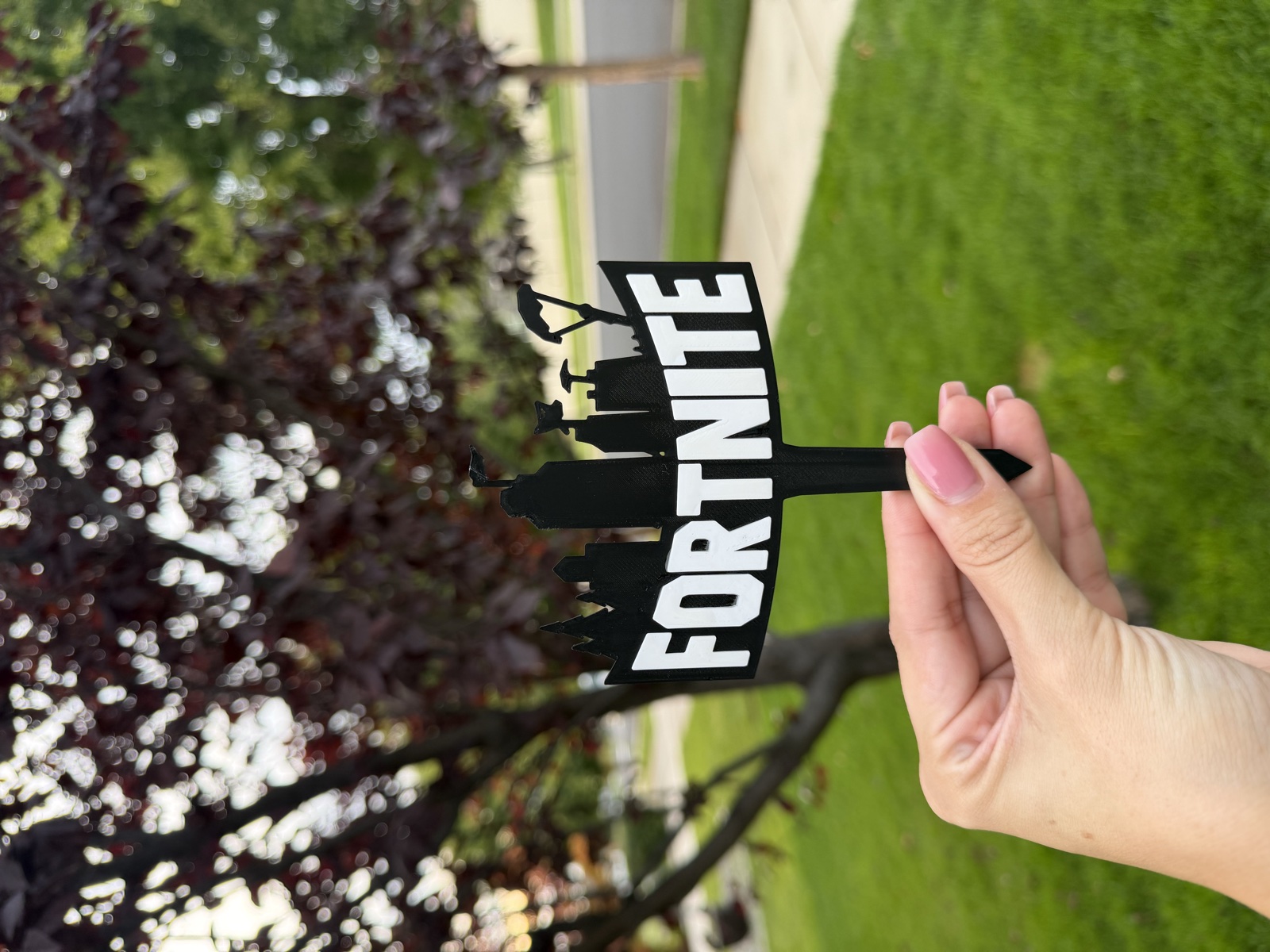 Black and white Fortnite cake topper held against a leafy outdoor background