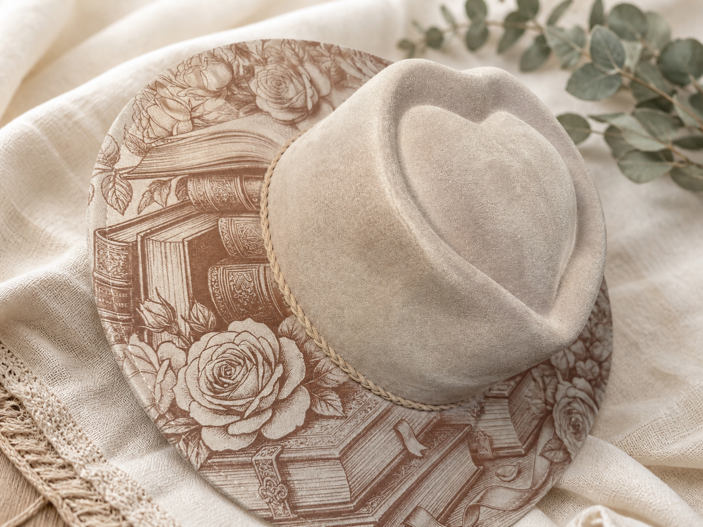 Angled view of a blush custom wide-brim hat with rose and vintage book artwork styled on soft ivory linen