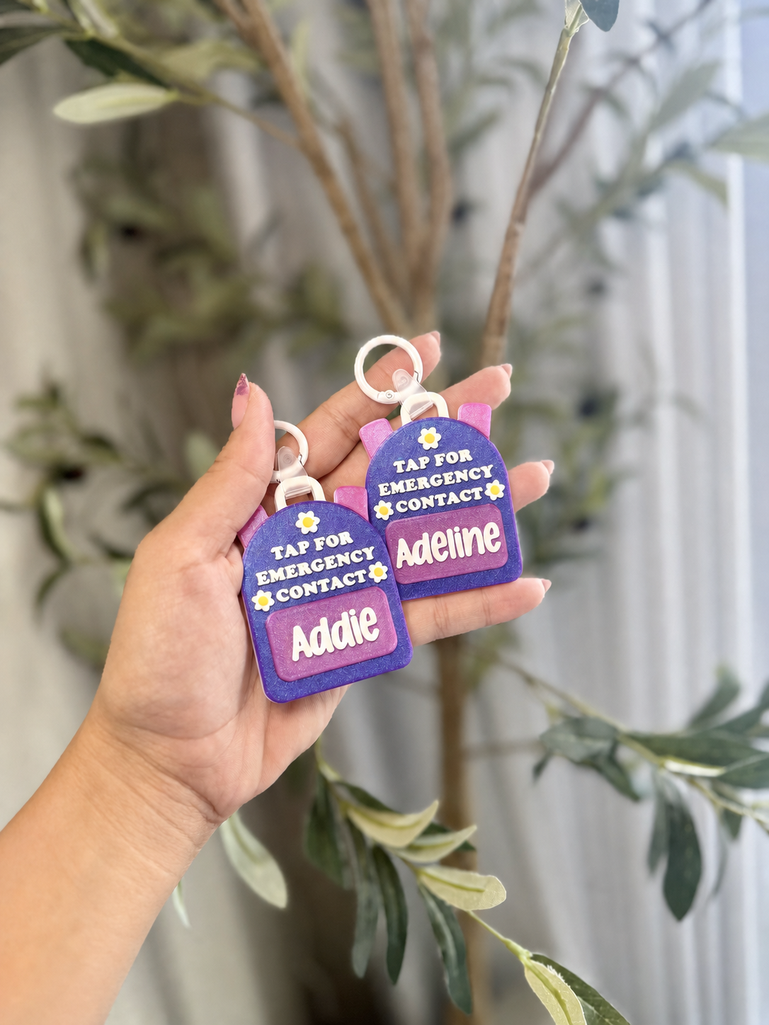 Two personalized purple backpack-shaped NFC emergency contact keychains held in one hand