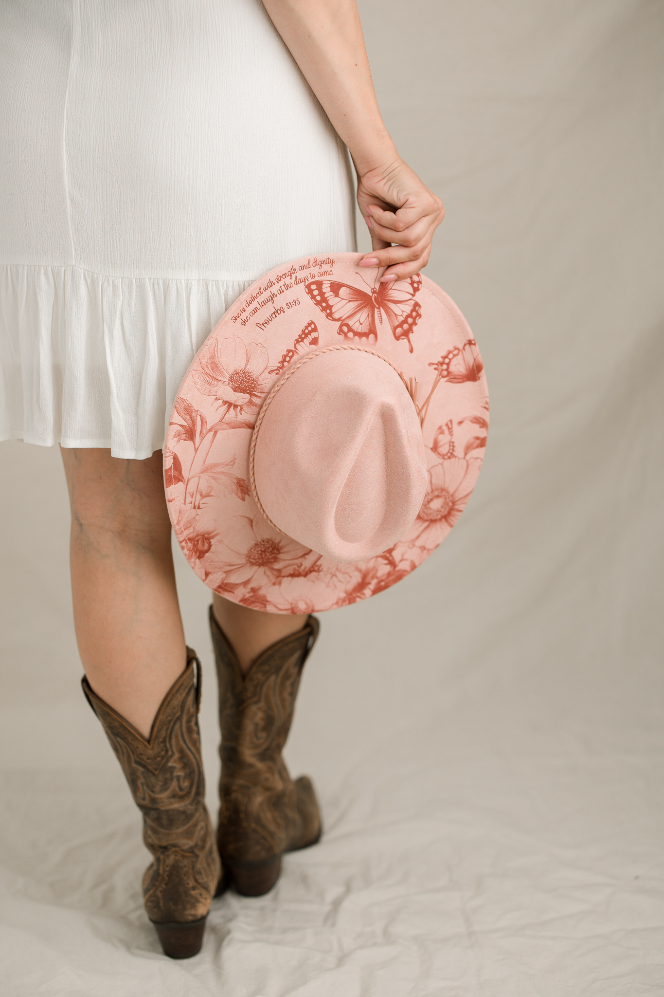 Blush butterfly and floral hat held beside a white dress